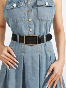Detail of a vintage black embossed leather belt with a carved gold metal buckle on denim