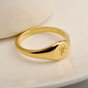 Macro shot of gold stainless steel signet ring with engraved star design on white ceramic