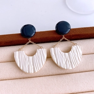 Detail of U-shaped white resin earrings with pleated texture and blue stud detail