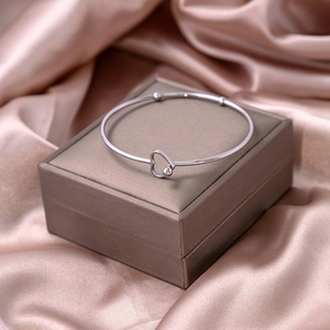 Polished silver heart knot open bangle displayed on a luxury jewelry gift box