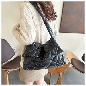 Detail of a black quilted shoulder bag with padded strap worn by a model in a soft setting