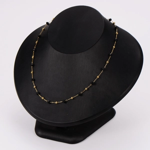 Collier en chaîne dorée avec perles noires présenté sur un buste d'exposition noir