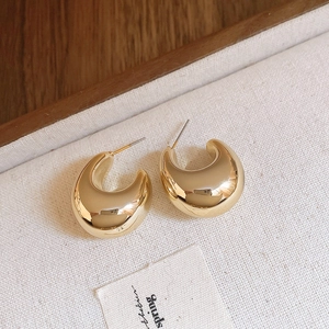 Vue rapprochée de boucles d'oreilles en C dorées sur un tissu à texture naturelle