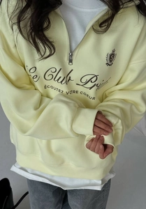 Detail of light yellow half-zip sweatshirt featuring a classic chest logo and letter print