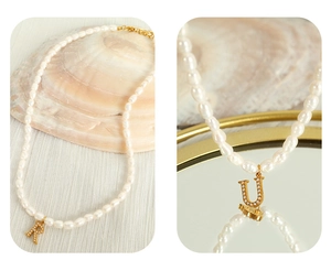 Detailed close-up of Baroque pearl necklace with gold letter pendants and lobster clasp