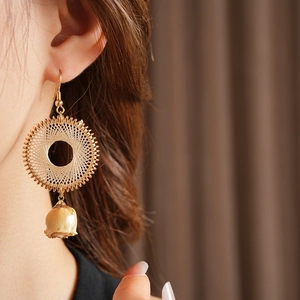 Detail of gold circular woven earring with a dried rose bud pendant on model