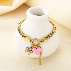 Gold stainless steel bracelet with pink heart and crystal flower charms on a ceramic vase