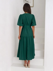 Back view of a deep green tiered midi dress with puff sleeves on a minimalist staircase
