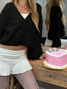 Detail of a black V-neck knit cardigan paired with a white pleated mini skirt and mesh tights