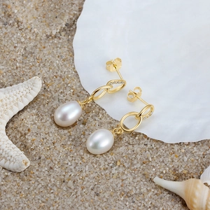 925 silver pearl drop earrings with gold hoops on sea shell and beach background