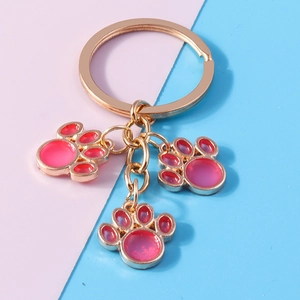 Close-up of golden cat paw keychains with pink gradient resin charms on colorful background