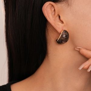 Detail of dark grey marble resin earrings with gold trim on model side profile