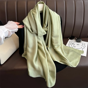 Close-up of light green satin scarf with smooth texture hanging on a black hanger