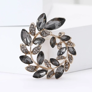 Macro shot of a golden laurel wreath brooch featuring dark grey and clear crystals
