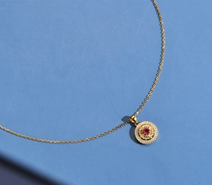 Detail of 18k gold plated silver necklace with hollow round pendant and red ruby center