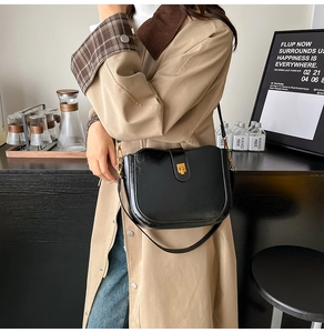Close-up of black glossy leather saddle bag with gold clasp on a trench coat model