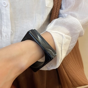Detail of square black marble acrylic bangle worn with an elegant striped blouse