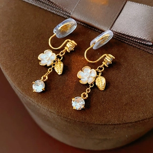Detailed close-up of golden flower clip-on earrings with zircon drop on velvet