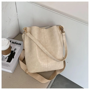 Detail of beige crocodile pattern bucket bag with wide fabric strap and gold hardware