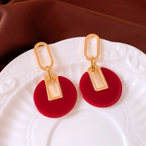 Detail of 18K gold plated hoop earrings with stylish red circular pendants on white tray