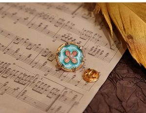 Macro shot of floral enamel brooch with pink clover and pearl on vintage music sheet