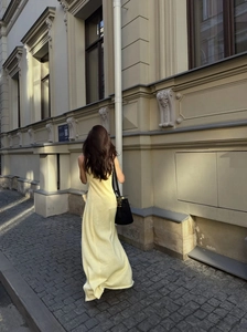 Back view of a long slim-fit light yellow knitted dress in a scenic outdoor street setting