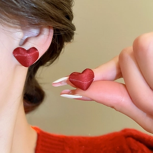 Dettaglio di orecchini a cuore rossi con trama satinata indossati da una modella