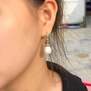 Close-up of pearl drop earrings with colorful zircon inlay on a golden hook