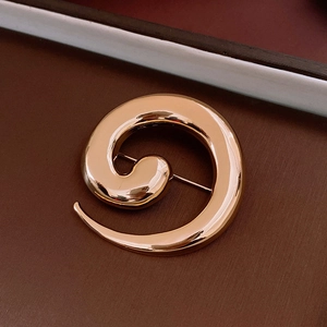 Macro shot of minimalist gold spiral metal brooch with smooth polished surface finish