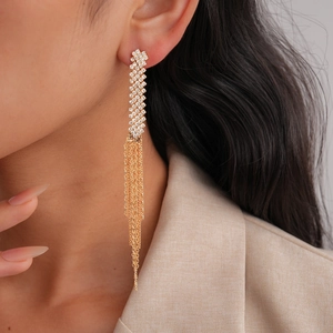 Close-up of golden tassel earrings with geometric crystal studs worn by a model