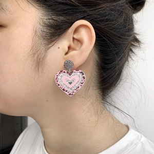Pink heart-shaped earrings with leopard print and silver glitter worn by a model