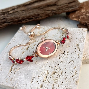 Detail of rose gold oval watch featuring a red dial and leaf-shaped gemstones