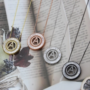 Macro detail of round letter A pendant with clear zirconia inlay in four metal finishes