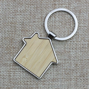 Detail view of a house-shaped wooden keychain with silver metal frame on linen