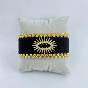 Detail eines handgewebten schwarzen Stoffarmbands mit goldenem Auge und Quasten