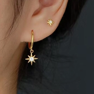 Macro shot of gold star hoop earring and stud with sparkling zircon on ear