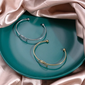 Close-up of gold and silver knot bangles on green ceramic dish over silk fabric