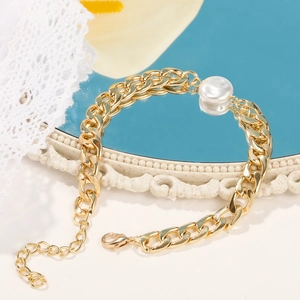 Close-up of gold chunky chain bracelet with large baroque pearl on a decorative mirror