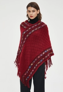 Detail of burgundy knit poncho featuring diamond patterns and multicolored fringe trim