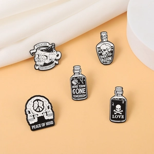 Set of gothic skull enamel pins including death potion and coffee cup motifs on fabric