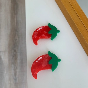 Detail shot of two shiny resin red chili pepper hair clips with green leaf stems