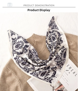 Detail of silk square scarf with damask pattern placed on a beige knit sweater