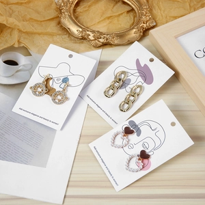 Three pairs of elegant gold earrings with Saturn, link, and heart motifs on art display cards