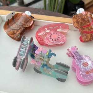 Détail de diverses pinces à cheveux en acrylique aux formes de téléphone et guitare