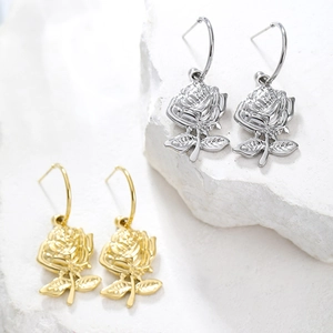 Close-up of gold and silver rose shaped earrings on white textured stone background