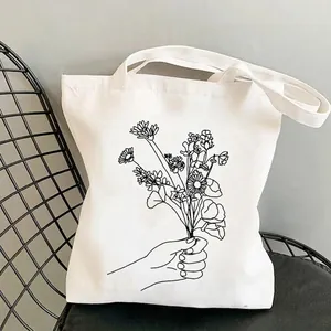 Minimalist wildflower garden canvas tote bag with black line art of hand holding flowers