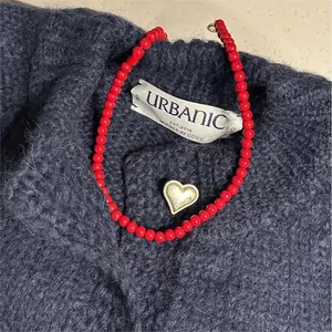 Dettaglio di una vivace collana di perle rosse con un ciondolo a forma di cuore in argento.