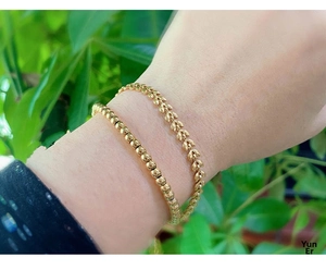 Detailed view of gold beaded chain and wheat leaf bracelet set worn on wrist