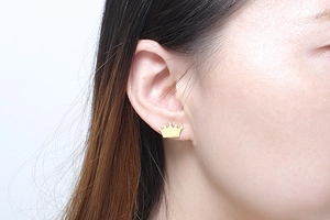 Close-up of a model wearing a small polished golden crown stud earring for women