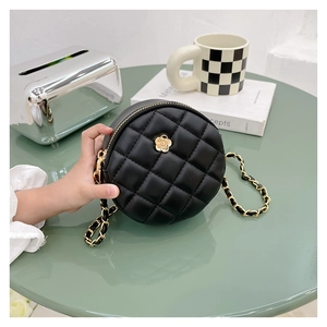 Detail of a black quilted round mini bag with golden camellia and chain strap